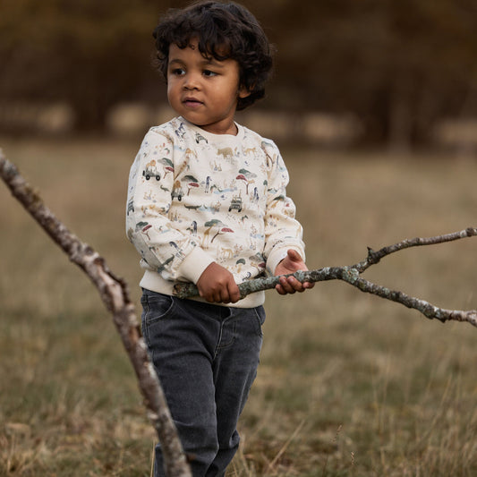 Kind trägt Little Dutch Pullover Beige mit Safari Print im Freien