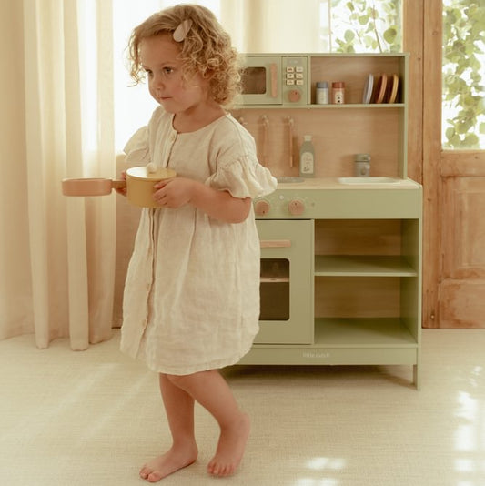 Kind trägt einen gelben Spieltopf vor der grünen Little Dutch Kinderküche.