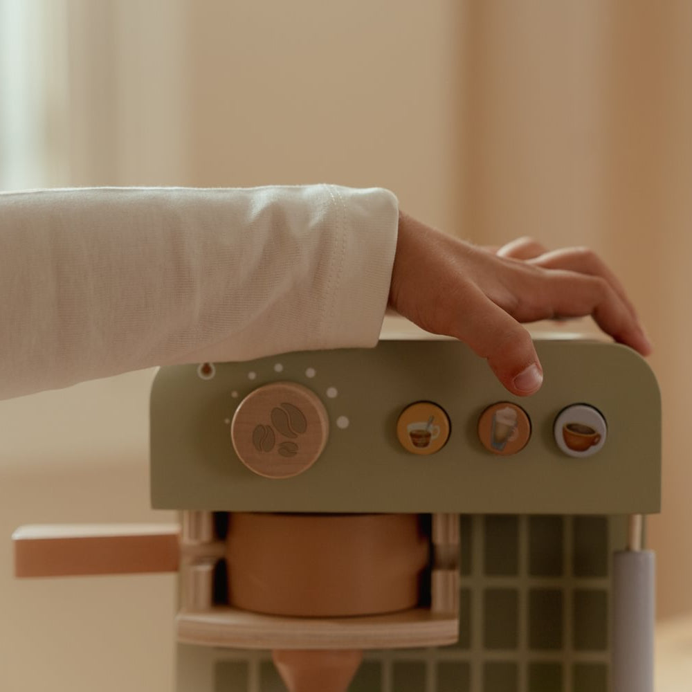 Kinderhand auf der grünen Little Dutch Kaffeemaschine über dem Drehknopf und den drei kleinen Knöpfen mit Getränkemotiven.