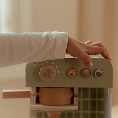 Kinderhand auf der grünen Little Dutch Kaffeemaschine über dem Drehknopf und den drei kleinen Knöpfen mit Getränkemotiven.