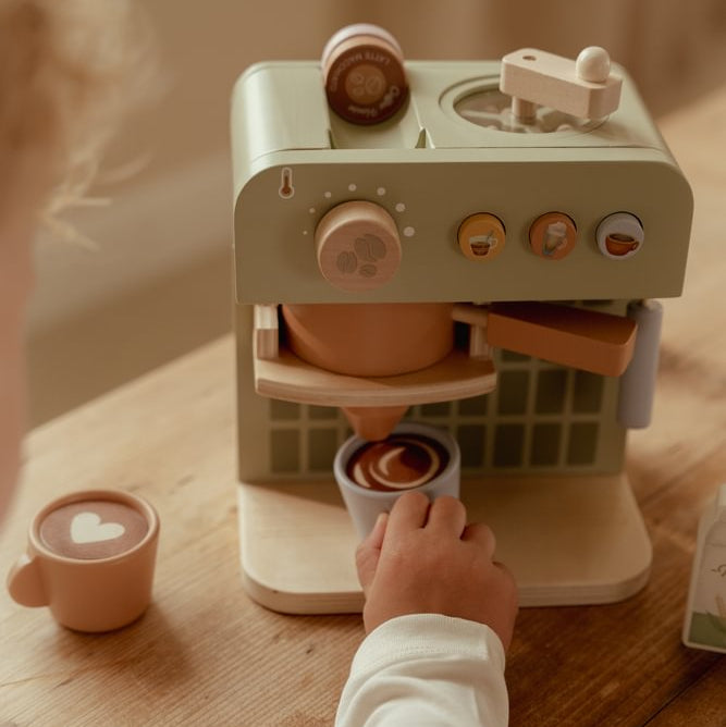 Kinder Barista - Kinderhand an einer hellblauen Tasse unter dem Auslauf der grünen Little Dutch Kaffeemaschine, daneben eine orangefarbene Tasse mit Herzmotiv.
