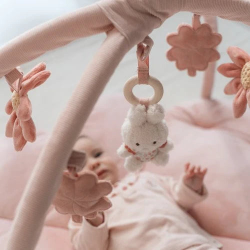 Baby greift auf der rosa Miffy Spieldecke Lucky Blossom nach einem hängenden Stoffkleeblatt.
